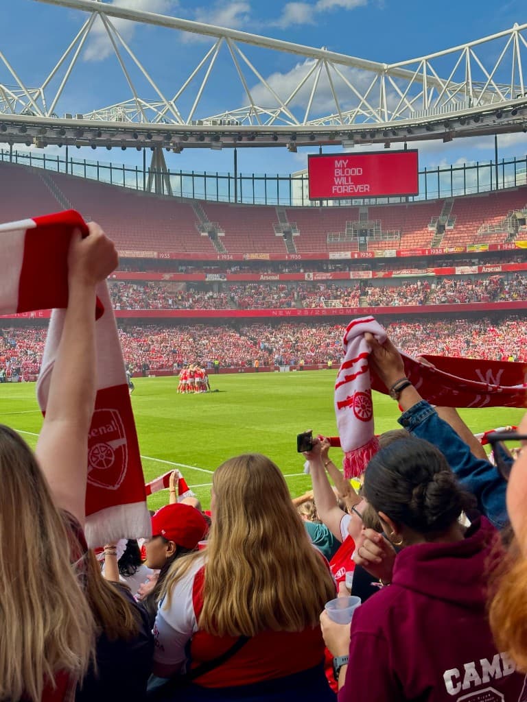 Fans in the stands at Emirates Stadium with Arsenal scarves and the pitch in view
